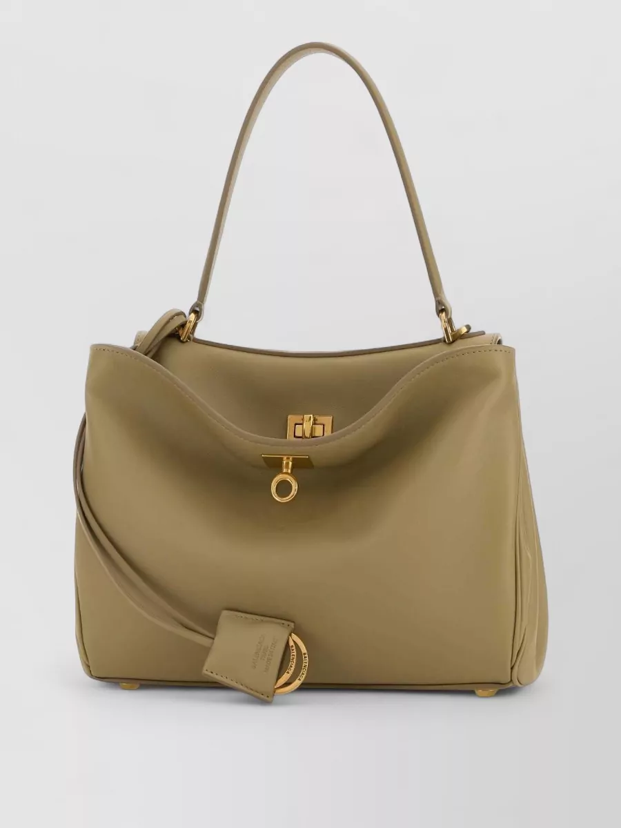 Balenciaga rodeo small leather shoulder bag — The nude-beige structured top-handle bag feels modern and sculptural yet discreet, its neutral tone balancing the dark suiting and cream heel for a cohesive, high-formality SS ensemble.