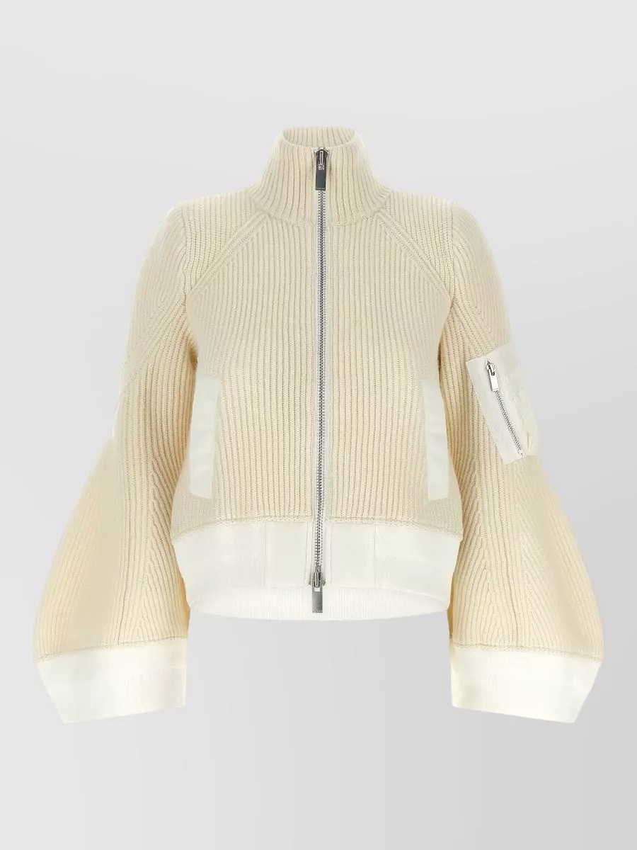 Sacai Wool ribbed cropped funnel-neck bell-sleeve jumper — The cream cropped zip knit with sculpted sleeves balances the coat’s dark faux fur with light contrast while matching its architectural, quiet-luxury volume and formality.