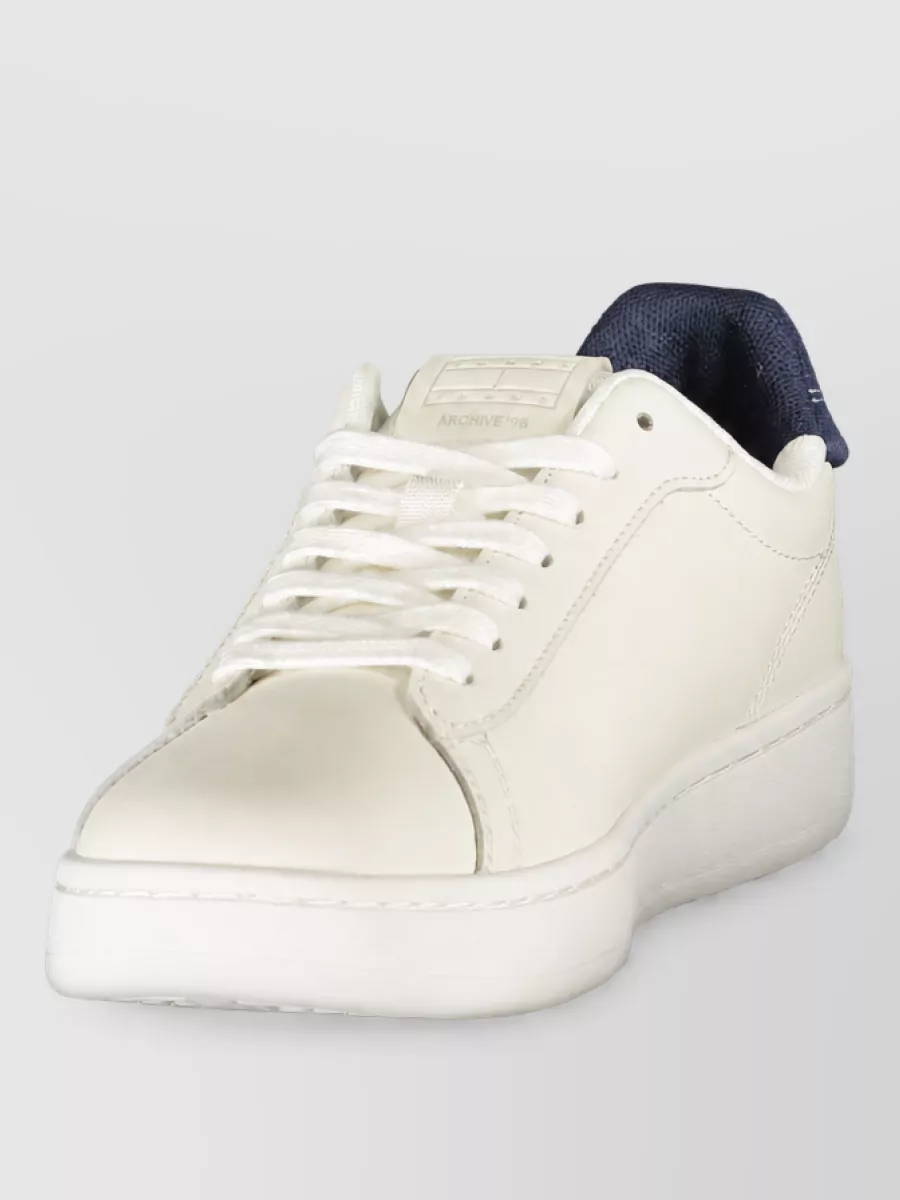 Tommy Hilfiger Leather lace-up sneakers — The off-white and navy sneakers echo the sweater’s winter white and Tommy flag tones, staying minimalist and preppy while matching the outfit’s casual-smart formality.