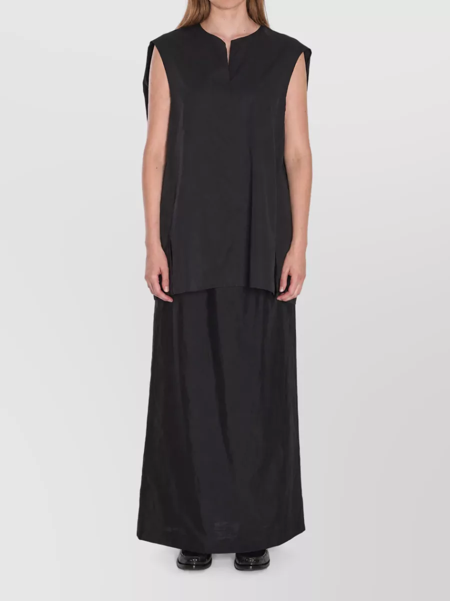 The Row Cotton oversized sleeveless blouse — The black longline tunic from The Row mirrors the skirt’s column line and fabric mood, creating a seamless, monolithic silhouette that feels quietly formal and gallery-to-dinner appropriate.