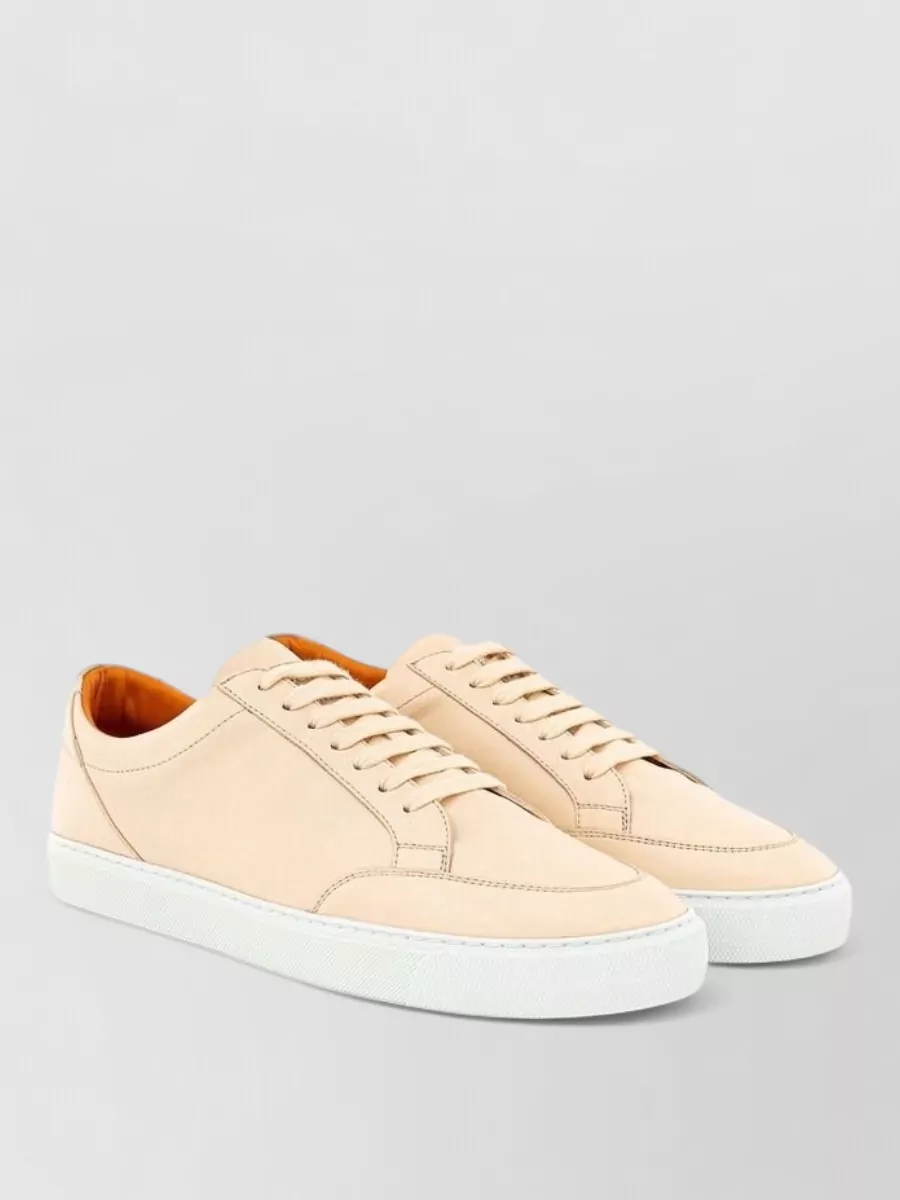 Burberry Leather low-top sneakers — The nude-beige leather sneakers are minimalist and refined, softening the black tailoring while nodding to Burberry’s beige heritage without adding more visible check.