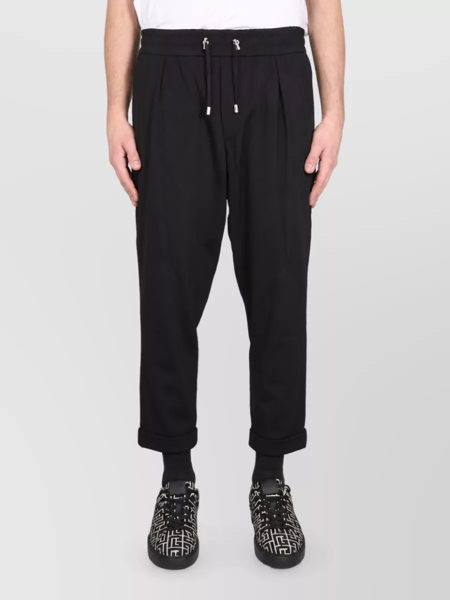 Balmain Straight-leg trousers — The black pleated drawstring trouser keeps the mood relaxed-luxe and streetwear, mirroring the tee’s quiet branding and balancing its blush tone with a clean, tapered line.