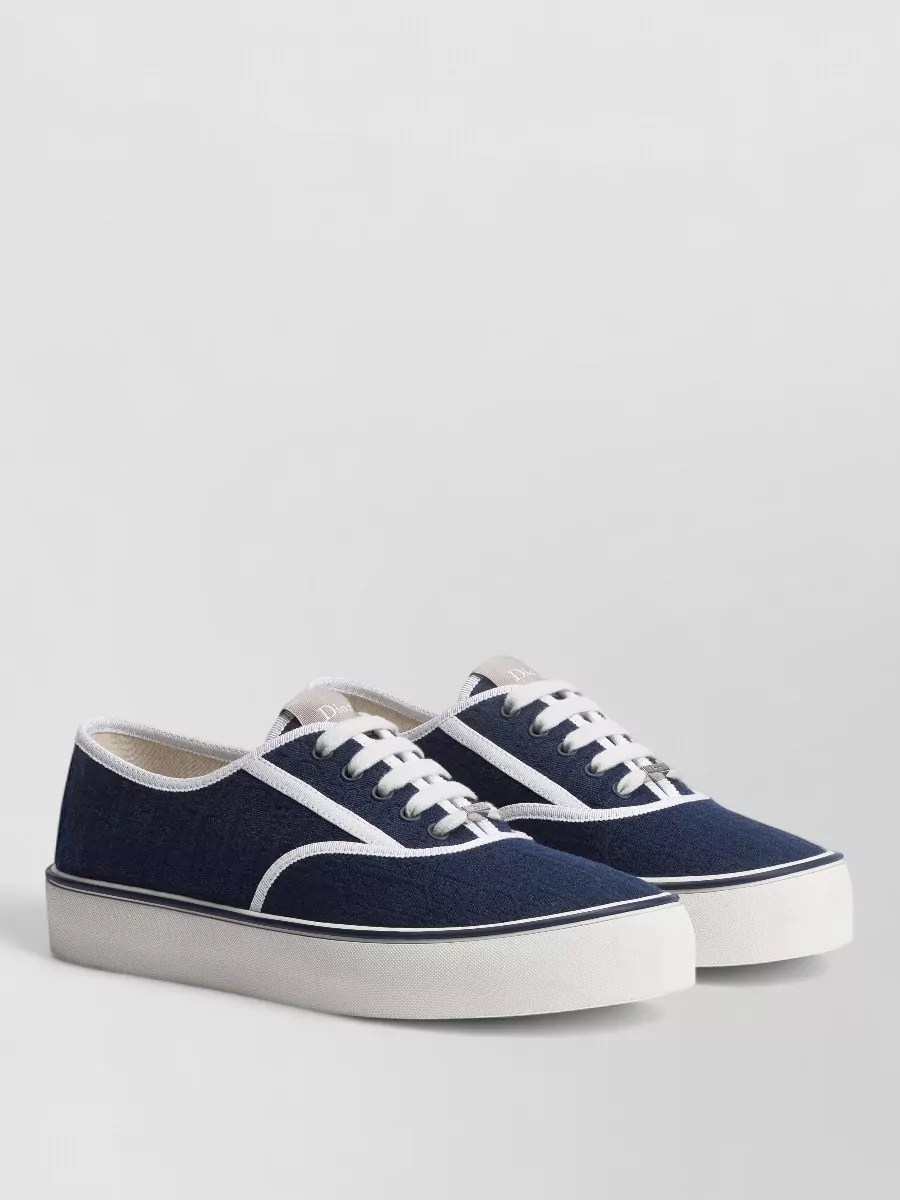 Christian Dior Leather lace-up sneakers — The Dior hiking-inspired ankle boots echo the workwear utility of the distressed shorts, stay in the same luxury tier, and the black/navy depth grounds the softer khaki and blue tones.