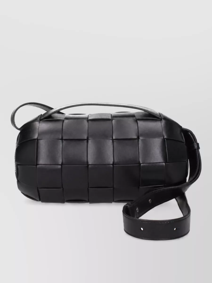 Bottega Veneta Leather clutch bag — The black intrecciato cylinder bag keeps to the dark monochrome base, adds rich texture, and feels proportionally right against the long coat and wide leg.