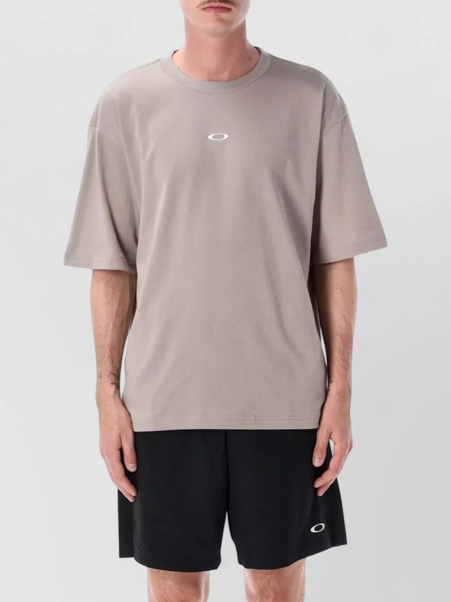 Oakley Printed short-sleeve t-shirt — The taupe Oakley tee keeps the outfit monochrome and technical, softening the black shorts while matching their minimalist sport mood and relaxed, easy proportions.