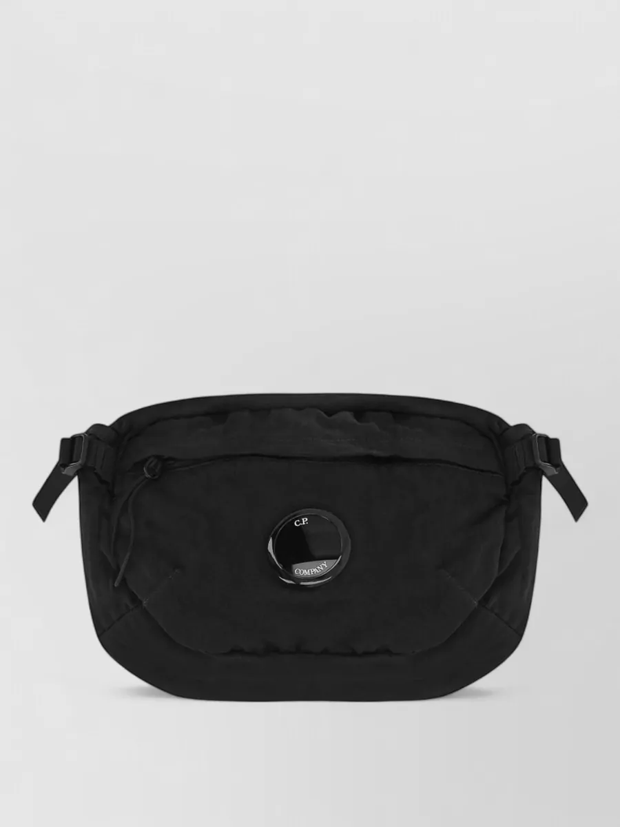 C.P. Company Quilted belt bag — The black C.P. Company padded crossbody adds subtle tech utility and hands-free practicality without fighting the bomber, and its compact scale sits well against the relaxed cargo-and-runner silhouette.
