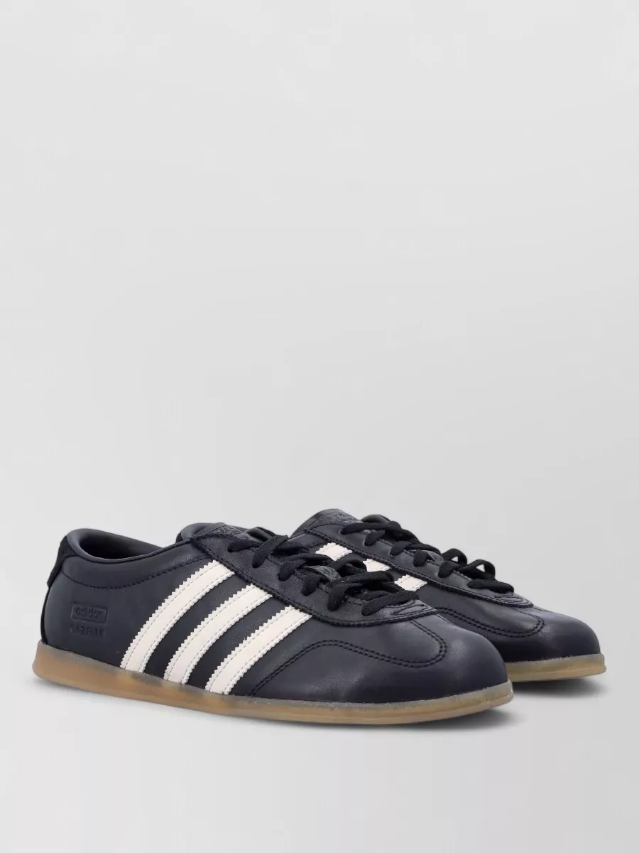 Adidas Originals Leather low-top sneakers — The navy Adidas Originals with off-white stripes and gum sole echo the skirt’s navy panels and sporty feel while staying slim enough not to visually shorten the mini.