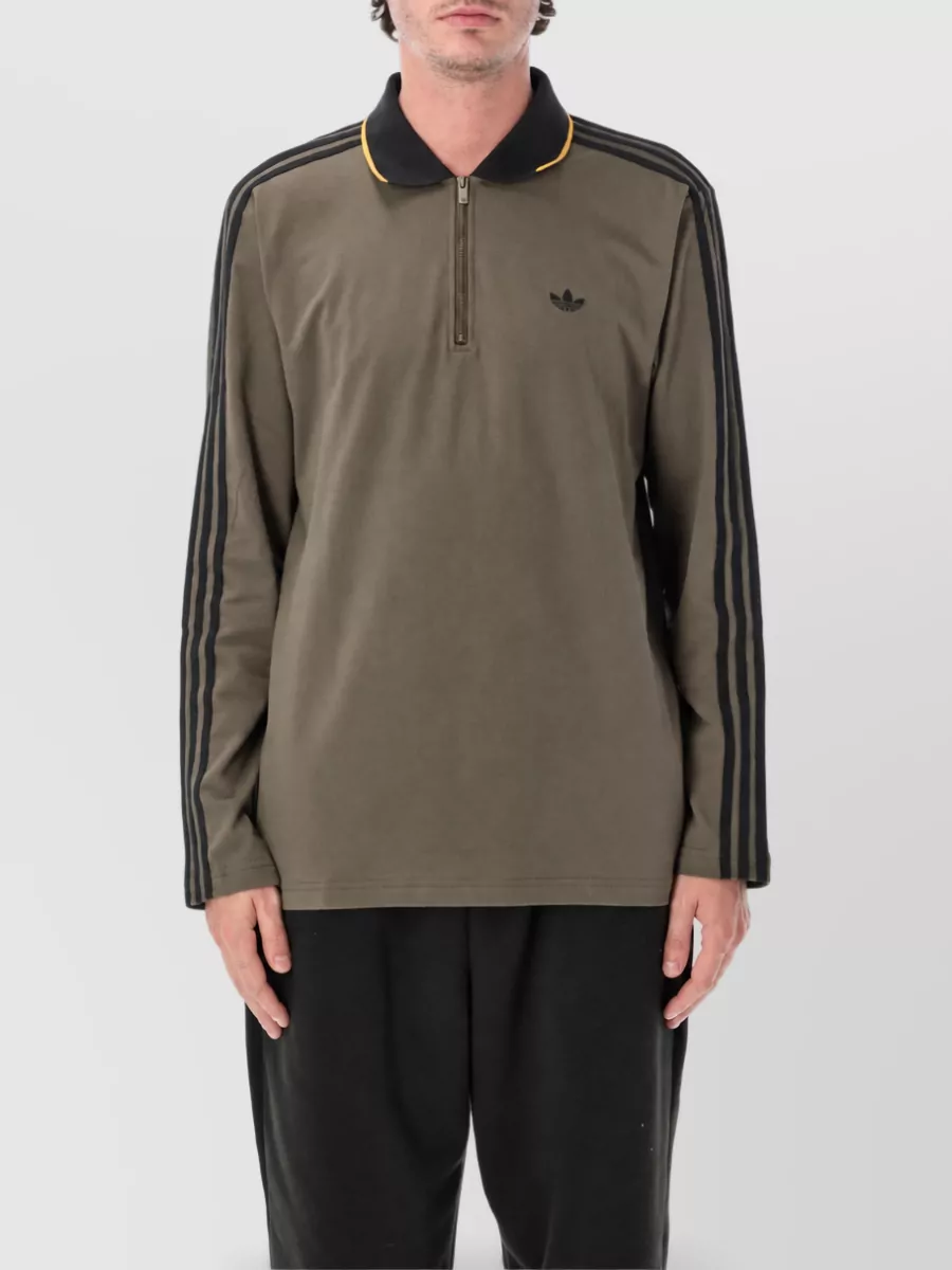 Adidas Originals Half zip polo t-shirt — The olive zip-neck polo keeps the Adidas stripes story, echoes the caramel and black of the jacket in a quieter way, and layers cleanly without competing with the outerwear.