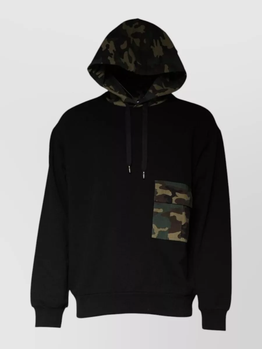 Dolce&Gabbana Camouflage hooded sweatshirt — The black hoodie with subtle camo hood and pocket echoes the jacket’s military theme without competing with its print, keeps formality casual, and layers cleanly under a padded parka.