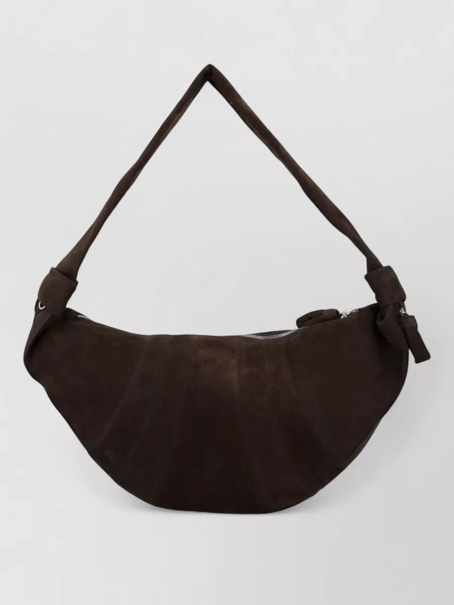 Lemaire Leather shoulder bag — The chocolate suede crescent bag echoes the boots’ warm brown and keeps the lines soft and sculptural, sitting harmoniously against the trench and knit dress without breaking the tonal depth.