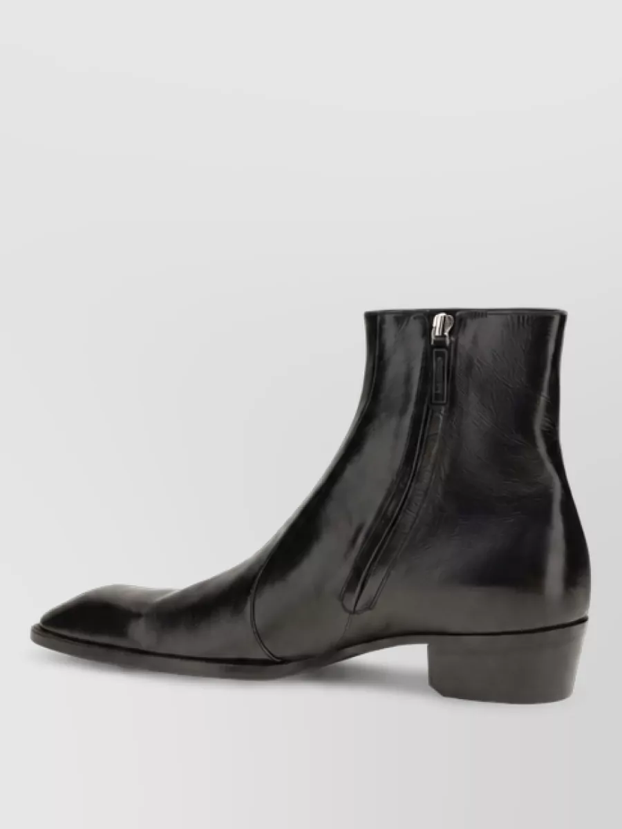 Saint Laurent Leather ankle boots — The sleek black ankle boot with a low block heel matches the jean’s slim-straight line and reinforces the brand’s rock-leaning quiet luxury while staying appropriate for smart-casual settings.