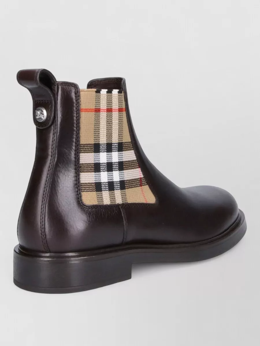 Burberry Leather ankle boots — The dark brown Chelsea boot sits right at the smart end of casual, grounding the beige trouser and harmonising with the warm tones in the Burberry check for a polished finish.