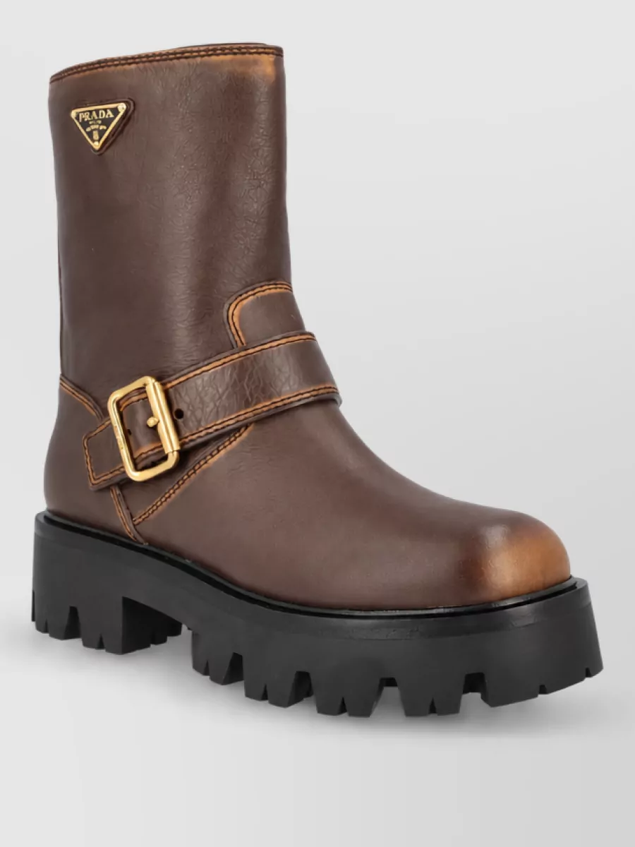 Prada Leather ankle boots — The chunky chocolate ankle boot with antique gold buckle ties directly into the knit’s metal charms and weighty attitude, giving a balanced, urban finish to the midi skirt’s movement.