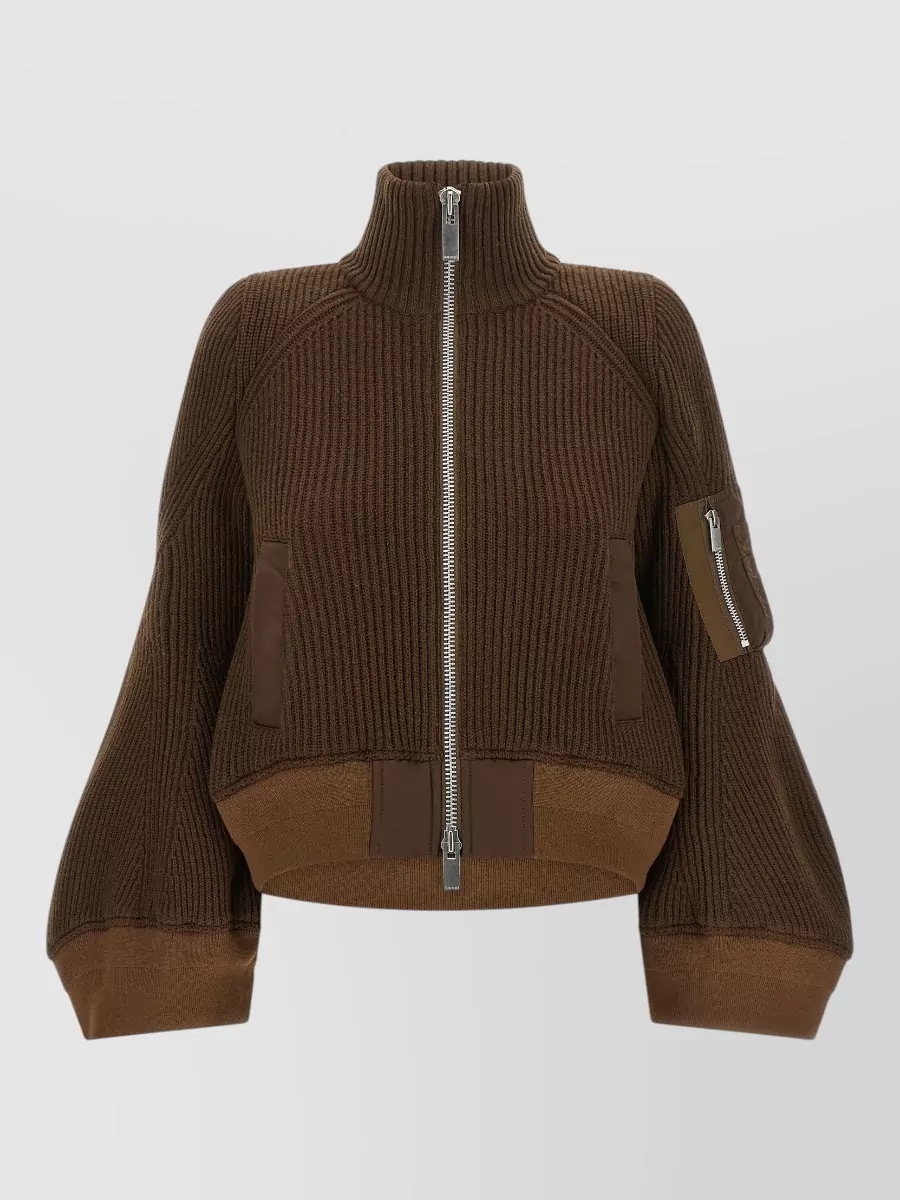 Sacai Wool ribbed cropped high neck zip jumper — The cropped chocolate Sacai bomber knit mirrors the parka’s utility tailoring and rich earth palette, layering cleanly under the short boxy coat without competing with its architectural volume.