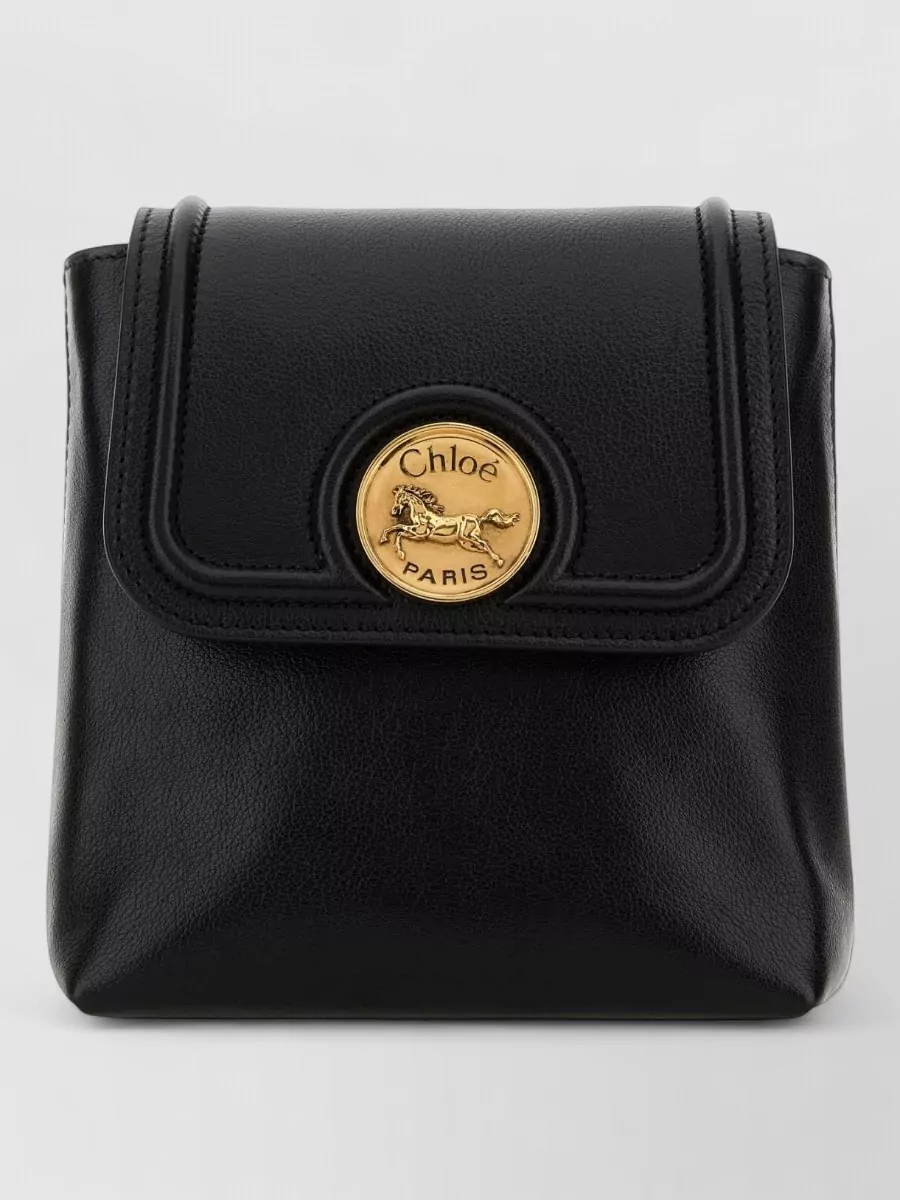 Chloé chain horse leather backpack — The compact black Chloé backpack mirrors the jacket’s black and gold hardware, keeps hands free, and maintains the quiet-luxury sporty attitude without skewing too technical.