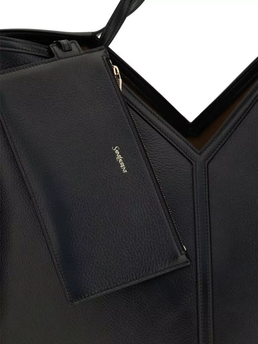 Saint Laurent Calf leather tote bag — The large structured black tote in H aligns with the tee’s quiet-luxury tier and adds a clean architectural note that works effortlessly with slim black denim and sneakers.