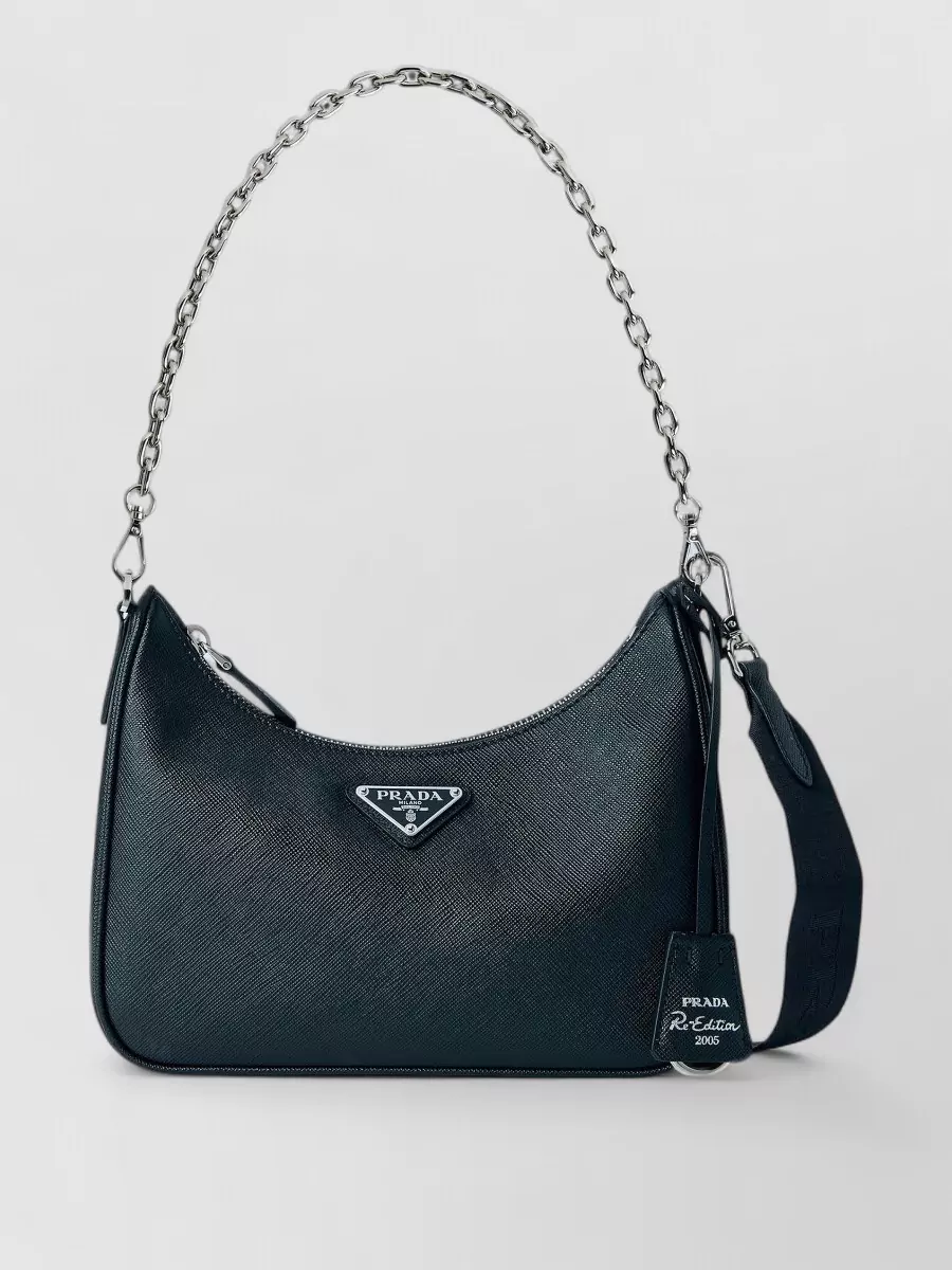 Prada re-edition leather shoulder bag — The Prada black crescent with silver chain keeps the palette tight, adds a sharp Y2K hardware accent, and balances the shine of the skirt and boots without competing.