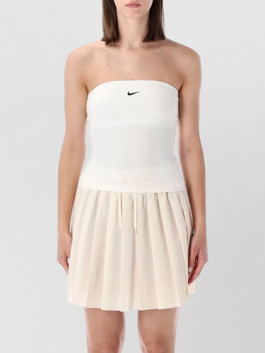 Nike Strapless fitted bandeau top — The beige pleated tennis skirt mirrors the stylist’s own pairing, keeping the black-and-ecru palette sharp and giving the slim ribbed tee a preppy, sport-forward contrast with a clean A-line line.