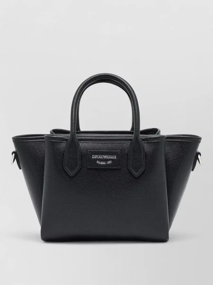 Emporio Armani Small tote bag — The structured black trapeze tote mirrors the clean tailoring and pairs seamlessly with the black loafer, delivering a cohesive, quiet-luxury desk-to-dinner pairing in both shape and tone.