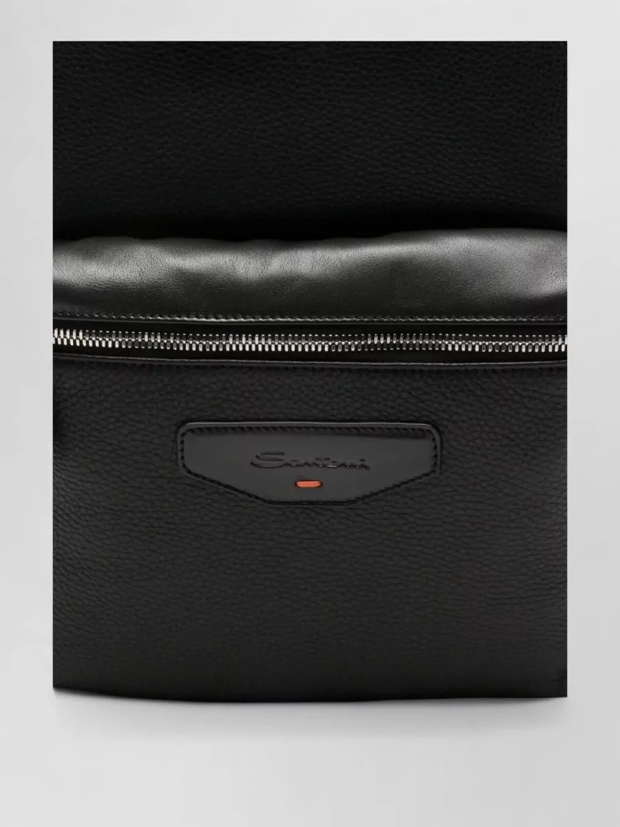 Santoni Leather backpack — The Santoni black leather backpack is streamlined and quietly luxurious, echoing the tailored mood while staying practical and understated against the monochrome base.