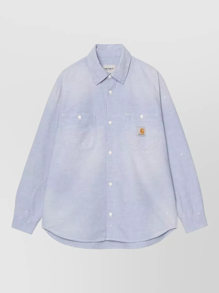 Carhartt Wip Denim long-sleeve painter shirt — The washed light-blue oxford work shirt mirrors the jeans’ mid-wash tone and relaxed skate attitude, creating a cohesive Carhartt workwear story with just enough character from the subtle paint splatter.