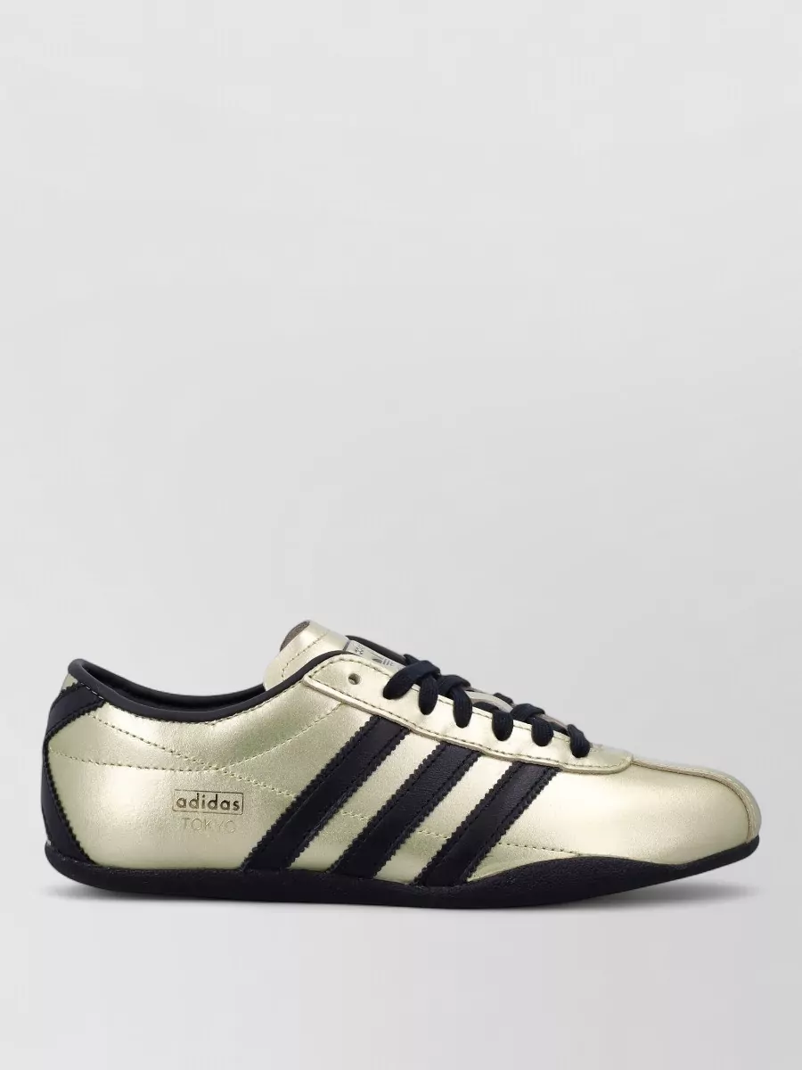 Adidas Originals Leather low-top sneakers — The metallic gold Adidas low-tops keep the outfit rooted in streetwear, echo the logo energy of the dress, and add a casual contrast to the bodycon silhouette while staying night-out ready.