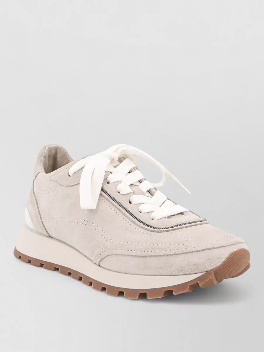 Brunello Cucinelli Suede low-top lace-up sneakers — The Brunello Cucinelli taupe runner reads refined and neutral, balancing the trouser’s structure with soft sport ease while keeping the palette muted around the cream knit.