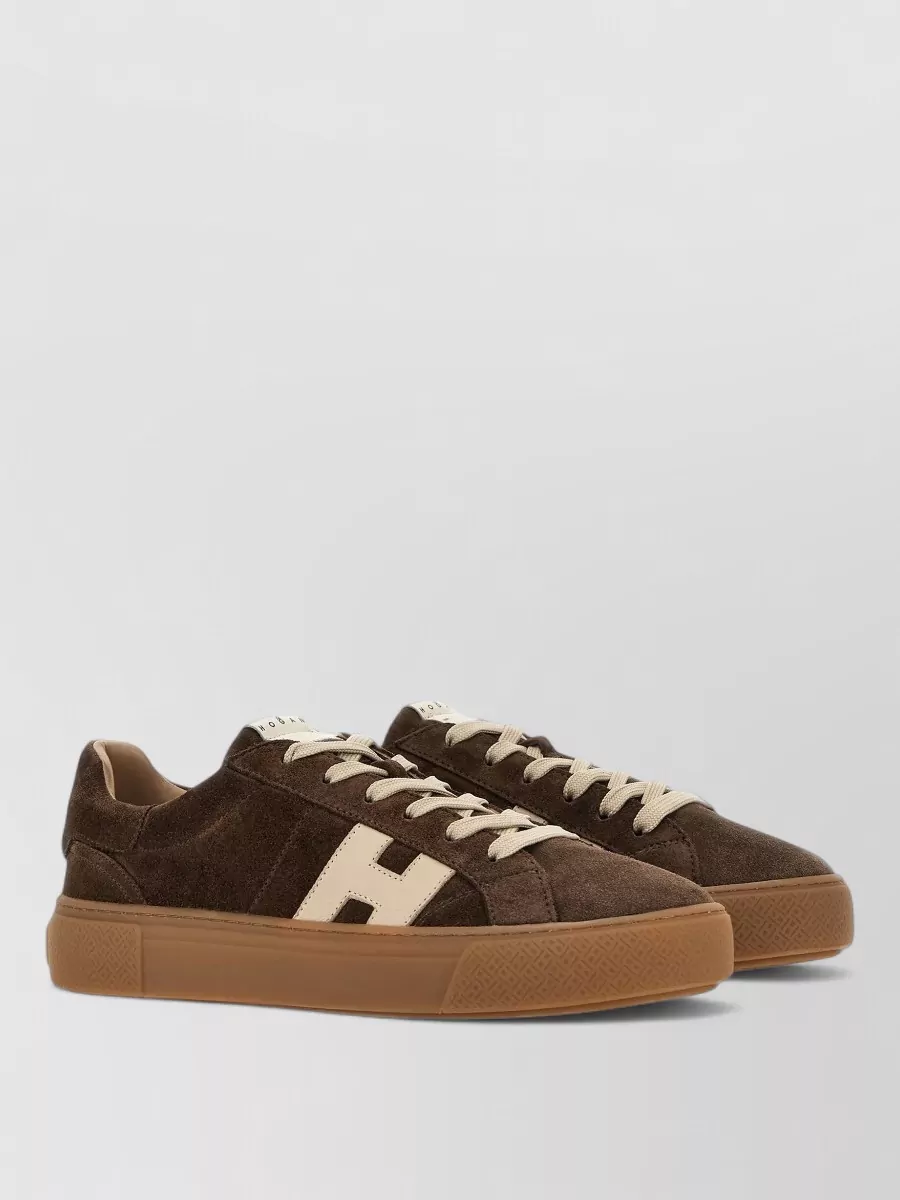 Hogan Leather low-top sneakers — Hogan’s chocolate suede sneaker with a caramel gum sole sits tonally with the brown tee and trouser while the gum base adds a subtle, modern contrast that still feels refined.