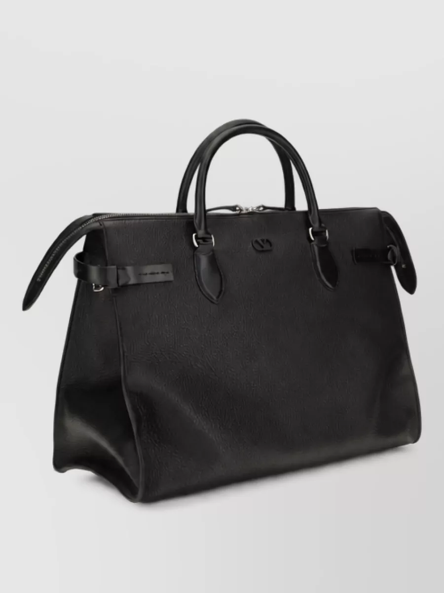 Valentino Garavani Leather top handle briefcase — Bag A, the structured black Valentino Garavani briefcase, mirrors the tailored rigor of the suiting and supports the boardroom-to-evening versatility of the outfit.