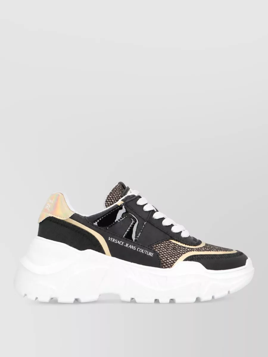 Versace Jeans Couture Leather low-top sneakers — The chunky black Versace Jeans Couture sneakers keep the outfit casual and balanced, echoing the black and gold details in the tee while grounding the ornate denim.