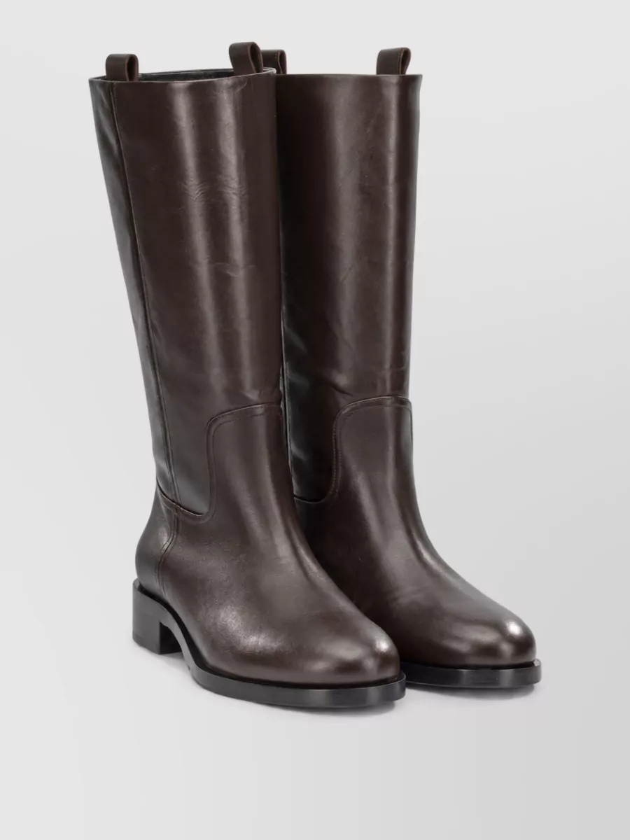 Aeyde Leather knee-high boots — The tall chocolate leather boot with a rounded toe grounds the A‑line midi perfectly, keeping the line long and calm while matching the skirt’s depth and formality.