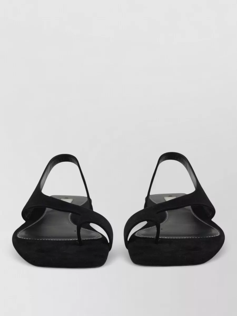 Totême Suede slides — The low-heel black slingback sandal echoes the source’s minimal sandal, adds a touch of lift, and keeps the mood quietly polished for city days through evening.
