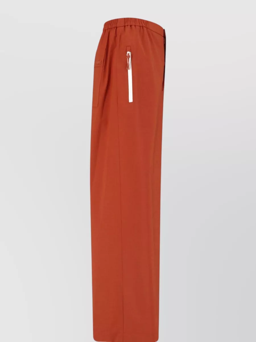 Lacoste Straight tailored shorts — The burnt terracotta Lacoste short adds a clean street-sport counterpoint to the bold rugby stripes, echoing the brick red while avoiding clashing stripes and keeping the silhouette relaxed and modern.