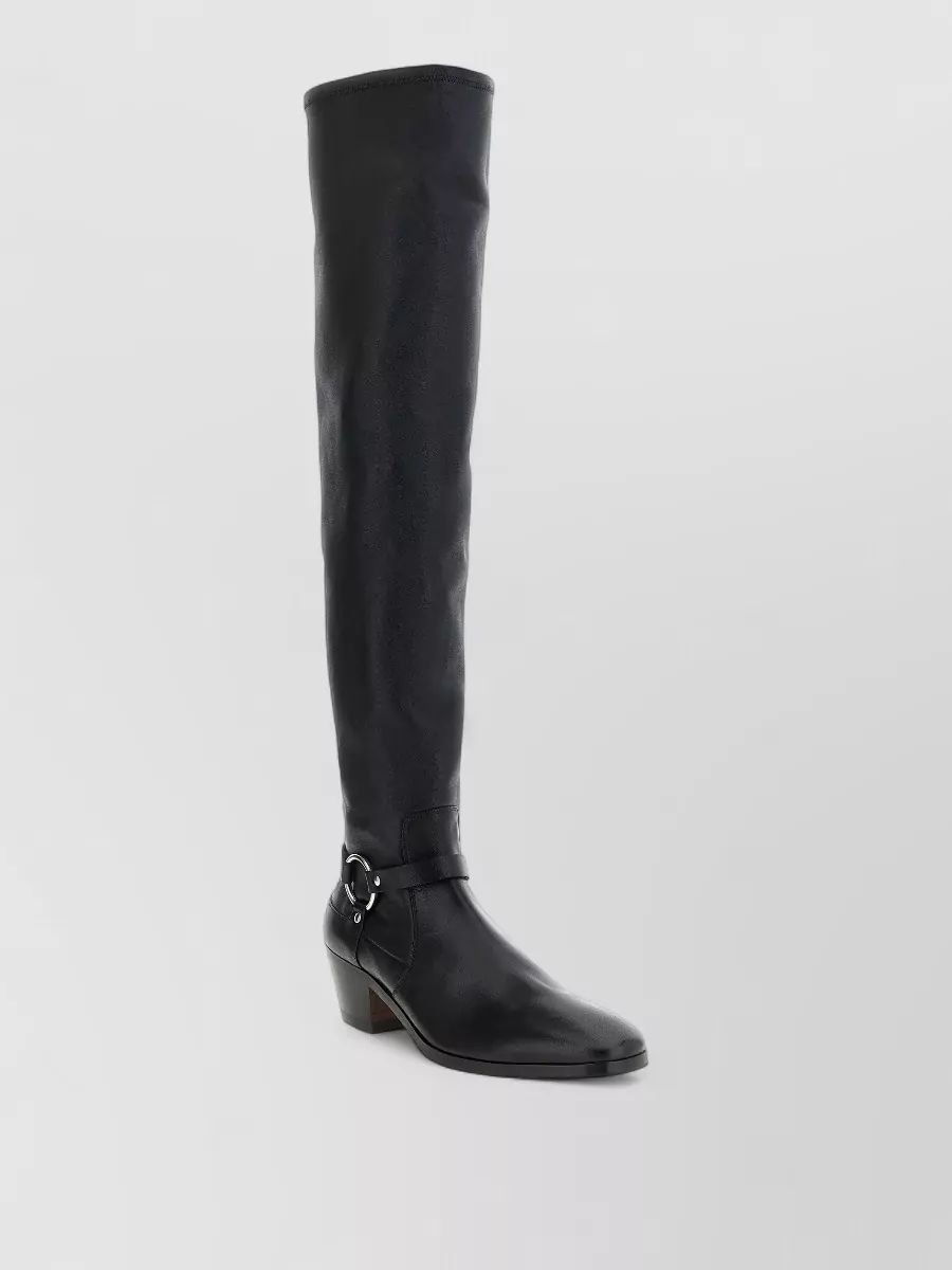 Tom Ford Leather over-the-knee boots — The over-the-knee black boots add a strong, continuous line under the midi dress, echo the jacket’s urban drama, and feel appropriately polished for its semi-formal quiet-luxury mood.