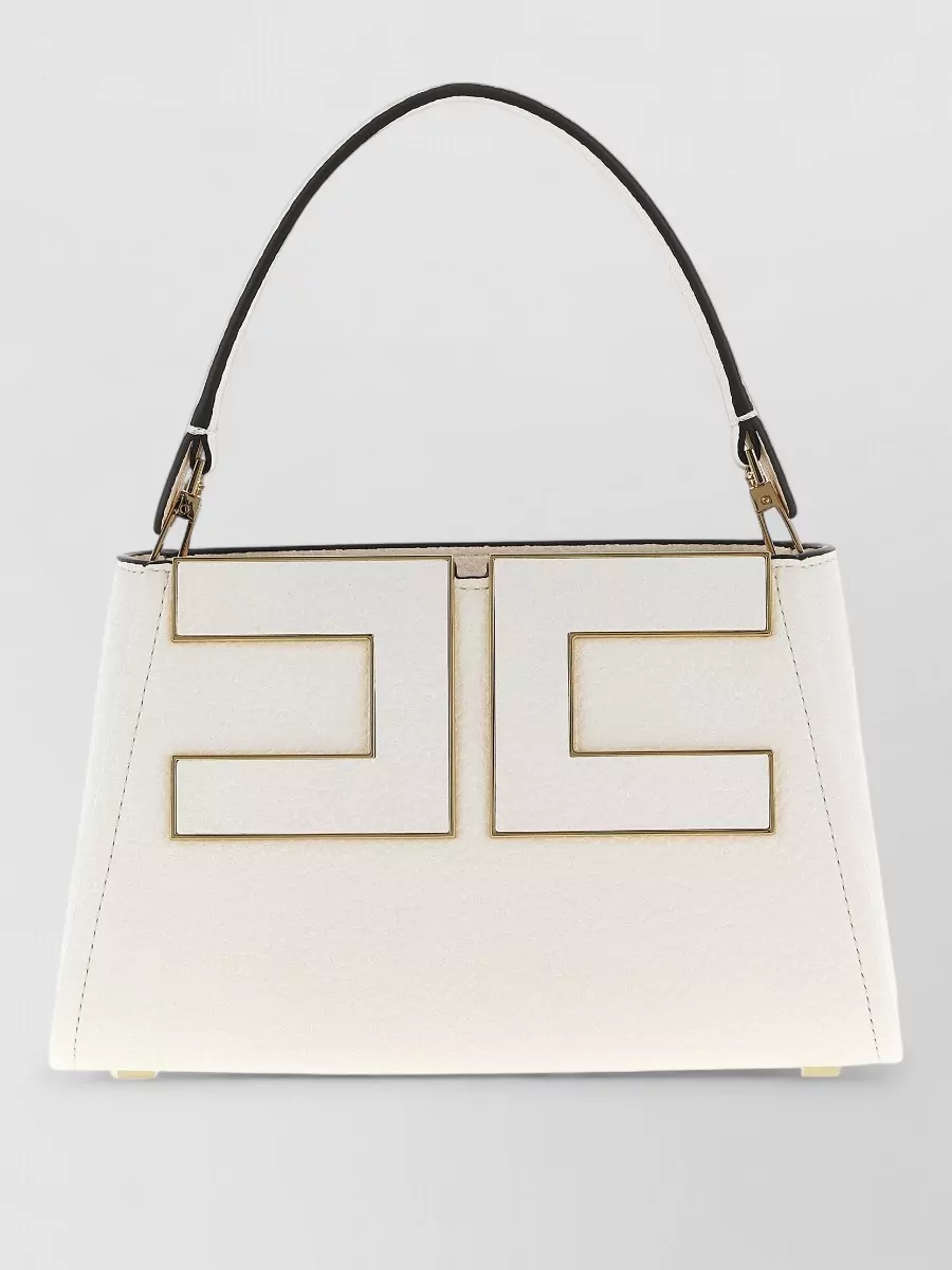 Elisabetta Franchi Textured faux leather shoulder bag — The ivory Elisabetta Franchi trapeze bag with pale gold accents brightens the navy ensemble and harmonizes with the gold buttons, staying in the same polished, quiet-luxury language.
