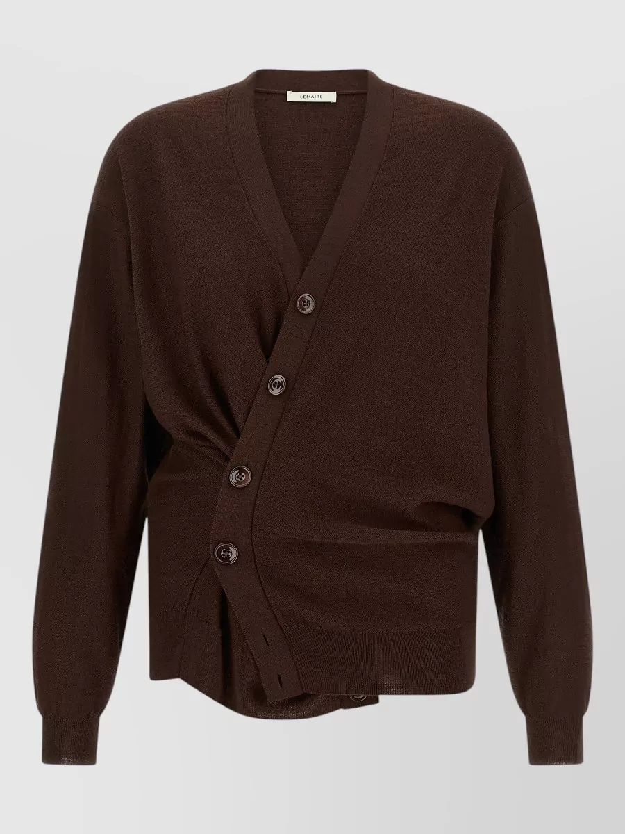 Lemaire Ribbed asymmetric wrap v-neck cardigan — The asymmetric dark chocolate cardigan echoes the coat’s cocooned tailoring and brown tonality while giving subtle structure at the waist, harmonising formality and palette for the outerwear.