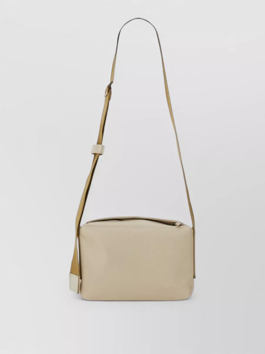 Uma Wang Leather crossbody bag — Our Legacy’s soft stone-beige cross-body quietly tracks the sandy neutrals and utility story, adding practical ease without breaking the light, monochrome balance.