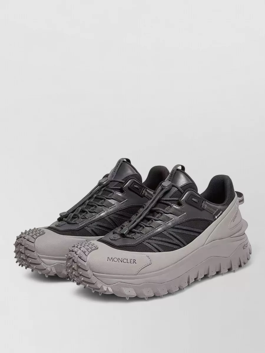 Moncler Leather low-top sneakers — The black and grey chunky trail sneaker echoes the technical vibe of the puffer and joggers, grounding the outfit in a performance-driven but urban-friendly way.