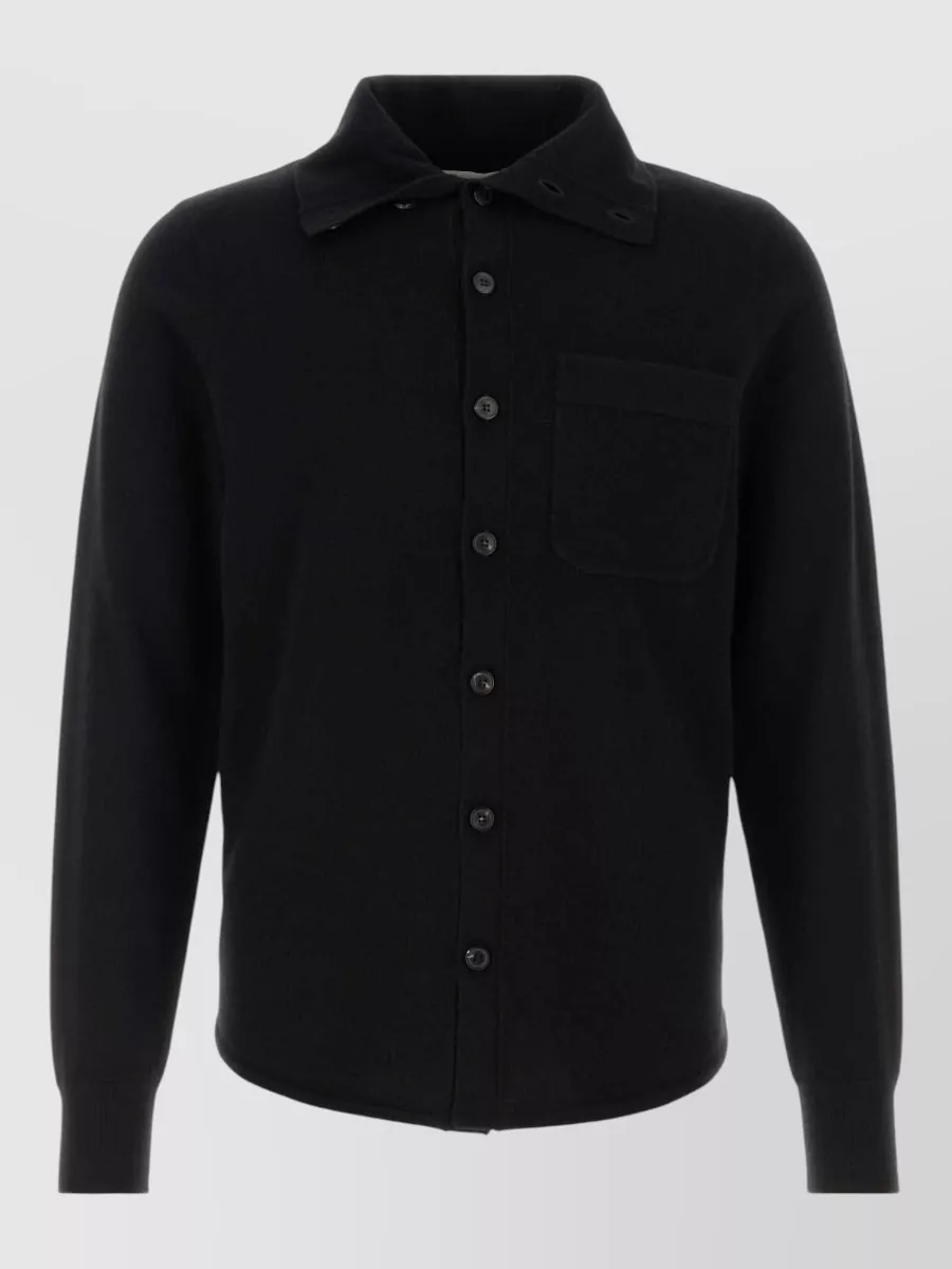 Dries Van Noten Cashmere monaco cardigan — The black knit shirt-cardigan keeps the palette seamless with the black wrap kilt, matching its quiet luxury mood while letting the directional bottom lead without competing tailoring up top.