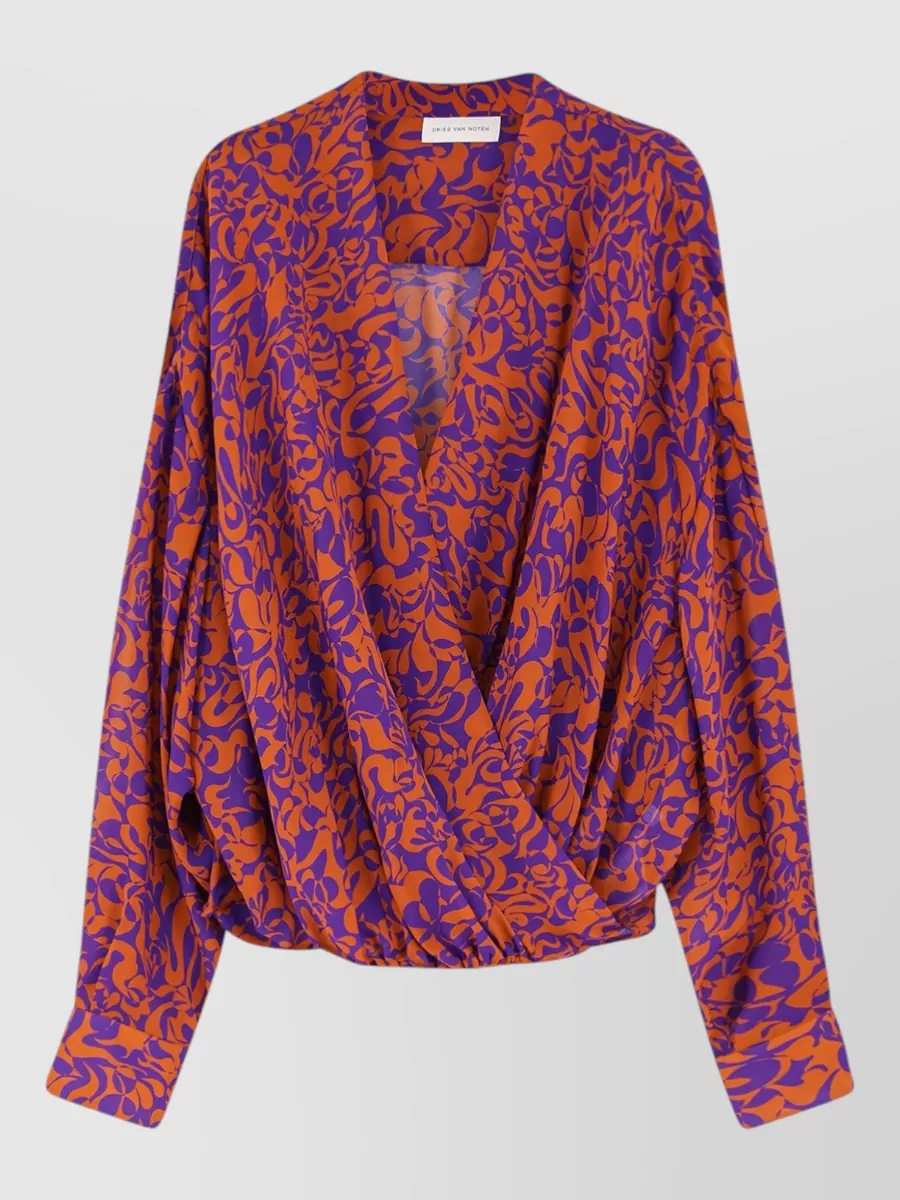 Dries Van Noten Printed blouse — The draped wrap blouse in the same purple‑orange geometric family echoes the skirt’s palette without repeating its ruffles, creating a cohesive but not matchy Dries set with a clean waistline.