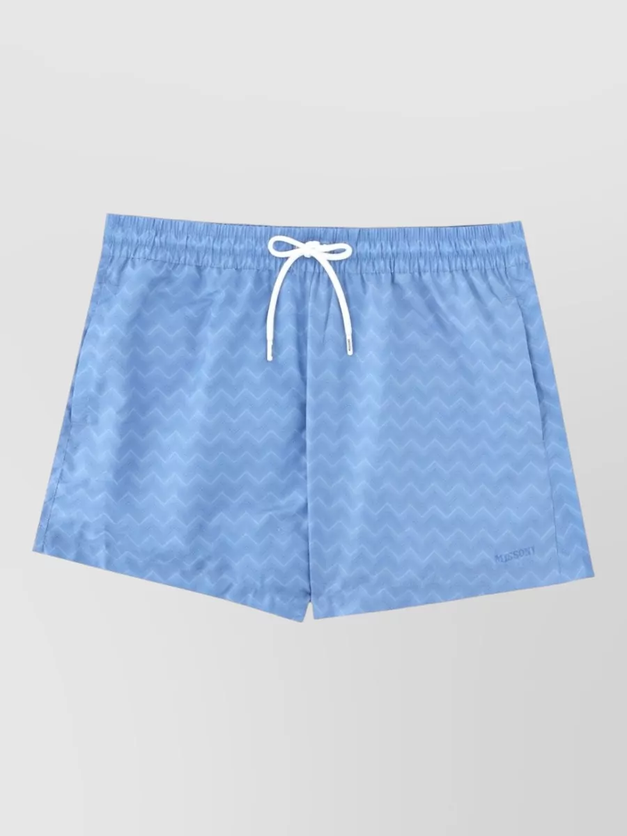 Missoni Printed swim shorts — The sky-blue Missoni deck shorts echo the tee’s bright azure in a softer tone, giving a clean, preppy sport set that feels considered without the chevron getting too loud.