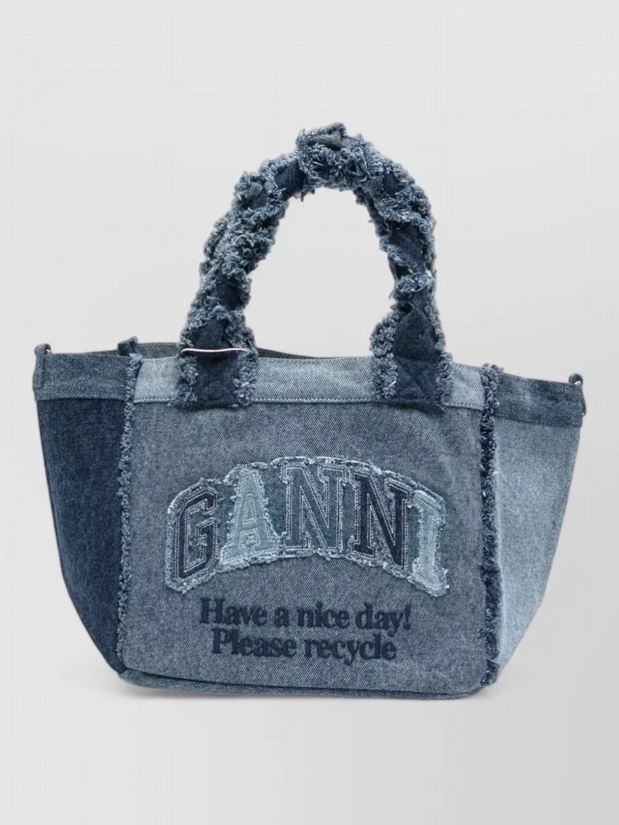 Ganni cabas small denim shoulder bag — The Ganni denim tote leans into the deconstructed, utility energy of the trousers, adding texture, capacity and casual ease while staying in a cool blue-grey spectrum that complements the stone base.