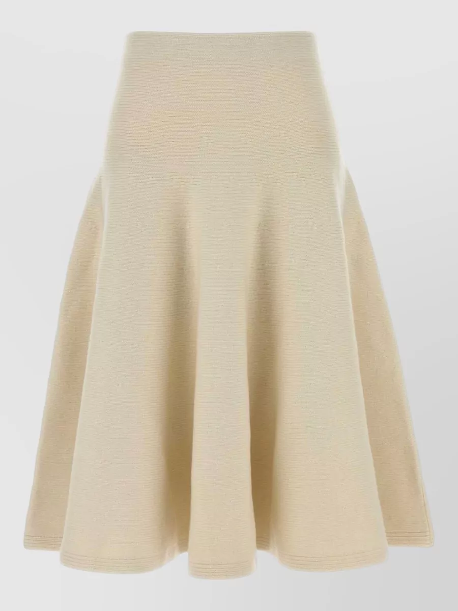 Alaïa Cashmere-blend knee-length skirt — The Alaïa buttercream knit midi mirrors the bag’s raffia-and-tan palette and quiet luxury mood, creating a minimalist, textural column that suits cooler seasons better than the more boho or beach-leaning dresses.