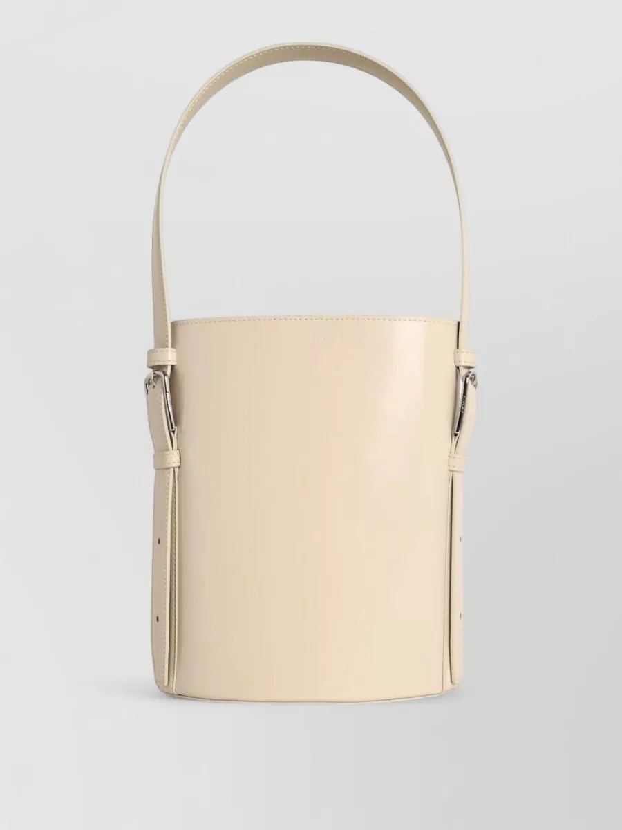 Coperni Leather bucket bag — The Jacquemus cream-beige crescent bag matches the warm neutral palette and refined evening vibe, adding a subtle gold accent without disturbing the minimalist line.