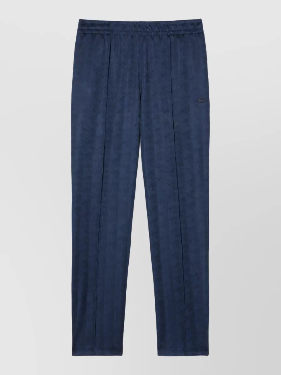 Lacoste Straight-leg trousers — The straight-leg navy jacquard track pant keeps the sports-preppy language consistent, grounds the light upper half, and balances the jacket’s short varsity cut with a clean, relaxed drape.