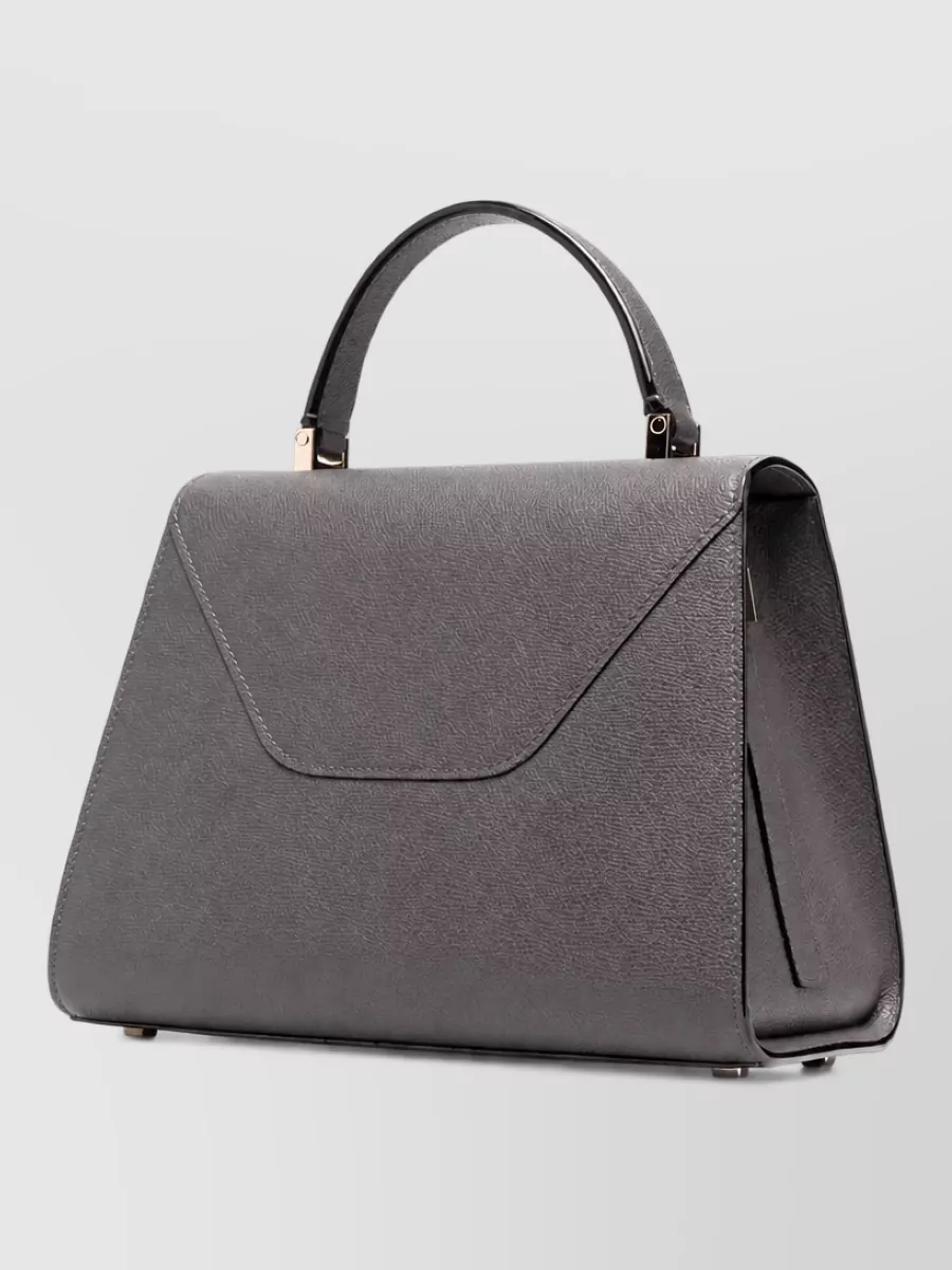 Valextra iside medium leather shoulder bag — The charcoal Valextra top-handle keeps to the cool grey-black palette and structured, tailored mood, adding a high-tier, architectural note that complements the wide-leg tailoring.