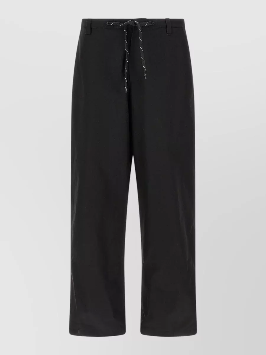 Balenciaga Cotton wide-leg trousers — The black straight-leg drawstring trouser mirrors the shirt’s tailored yet street energy, keeping the palette sharp and the silhouette relaxed without competing with the navy stripe.