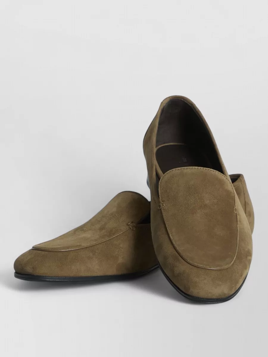 The Row Suede loafers — The Row’s taupe-olive suede loafers sit in the same understated luxury tier as the bag and dress, their soft neutral grounding the knit column with relaxed polish rather than sharp formality.