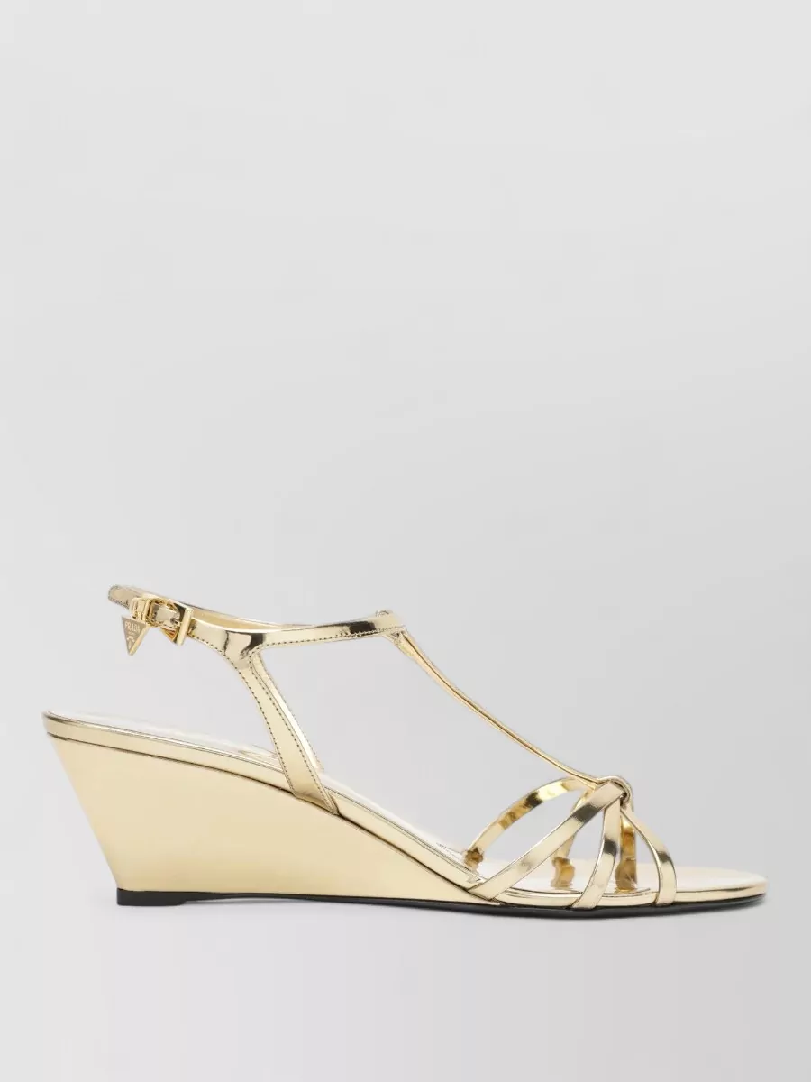 Prada Sandals — The Prada metallic gold wedge sandal matches the dress’s Pucci-glam brief, keeps the palette warm and neutral, and delivers cocktail-ready height without competing with the busy boho print.