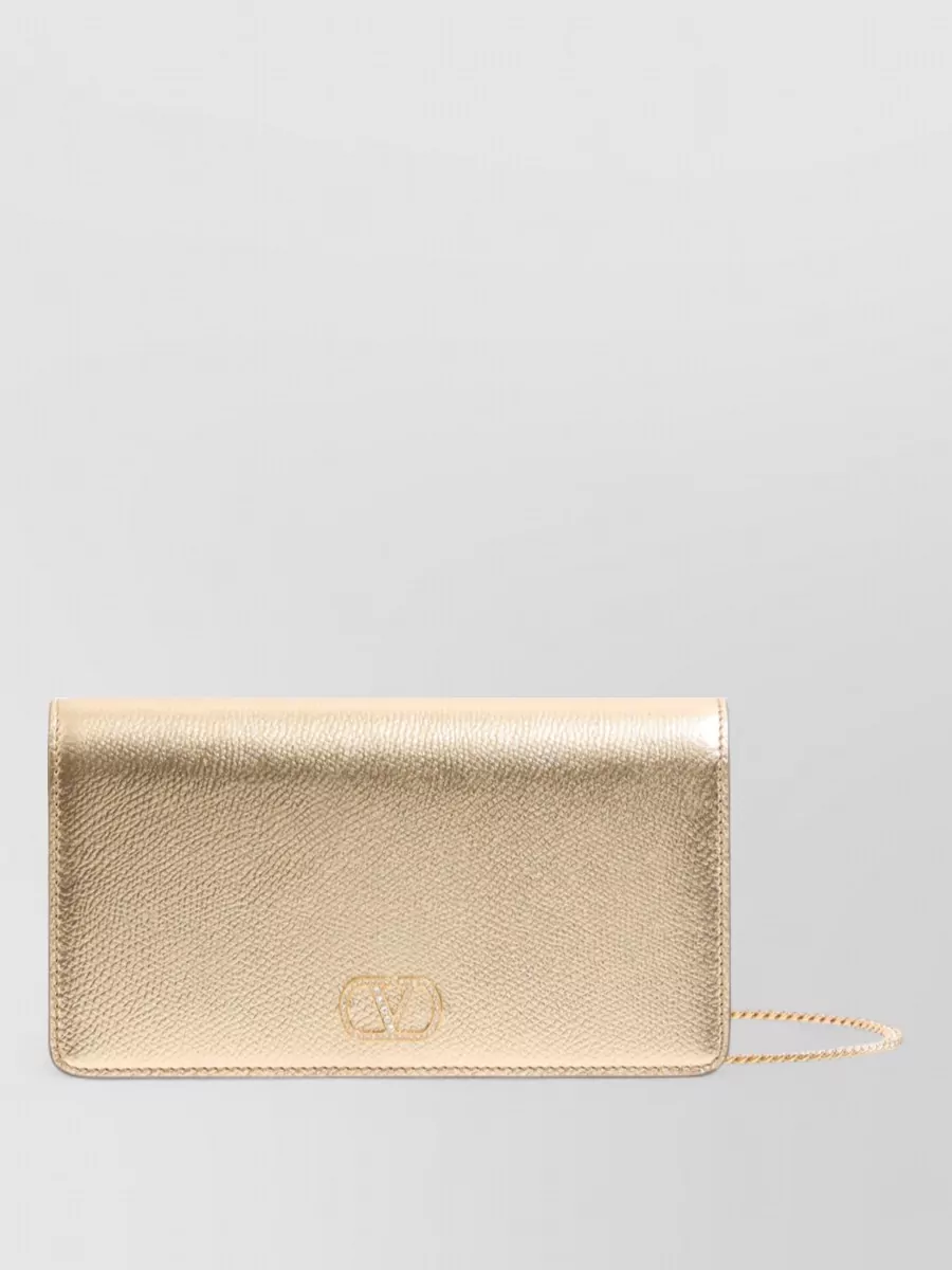 Valentino Garavani vlogo signature mini leather clutch bag — The Valentino light-gold clutch softly echoes the shoe’s metallic gold without competing, adding a romantic glow that complements the dress’s gold hardware and keeps the palette tight and luxurious.